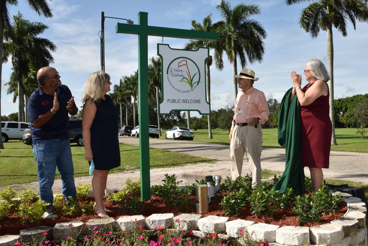 Golf participants next to course sign