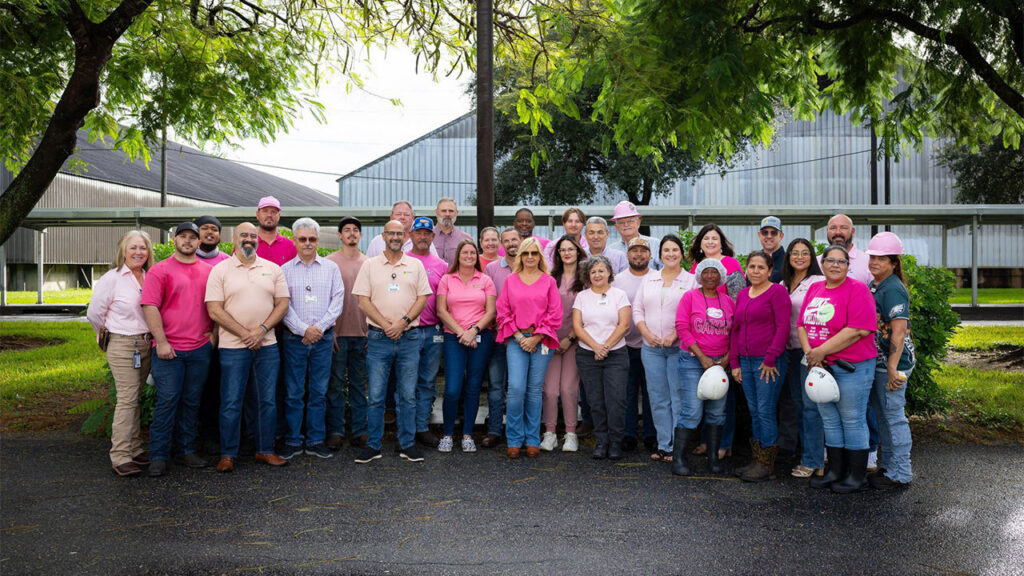 A large group of U.S. Sugar employees gather outdoors, many wearing pink to recognize Breast Cancer Awareness Month.