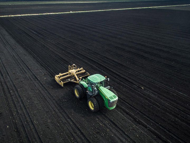 Tractor preparing dark agricultural soil in a South Florida field as part of sustainable farming and water quality practices.